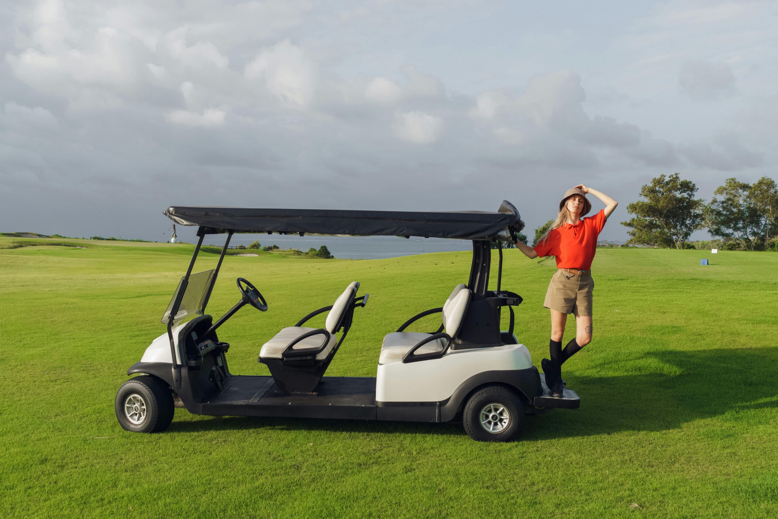 A woman in golf attire standing confidently beside a golf cart on a vibrant green golf course.